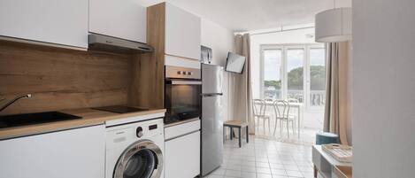 A modern kitchen with a washing machine, oven, and a TV mounted on the wall.
