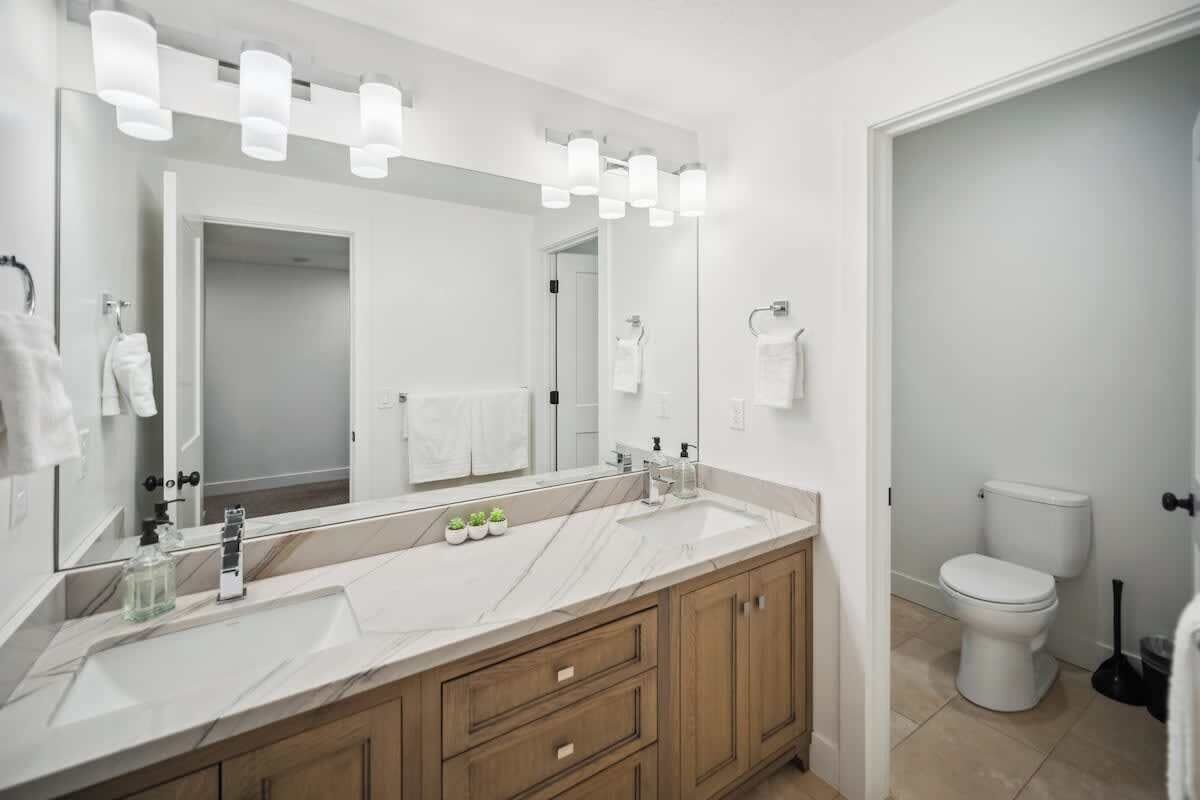 Un bagno moderno con uno specchio grande, due lavabi e un water.