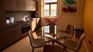 A modern kitchen with a dining area, featuring a glass table and chairs, a view of the sea, and a painting on the wall. - Valletta heart two, 3-room superior apartment (Valletta)