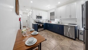 A modern kitchen with white cabinets, a stainless steel dishwasher, and a dining area with a wooden table set for two.