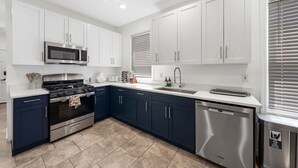 A modern kitchen with white cabinets, a stainless steel microwave, a gas stove, a dishwasher, and a window with blinds.