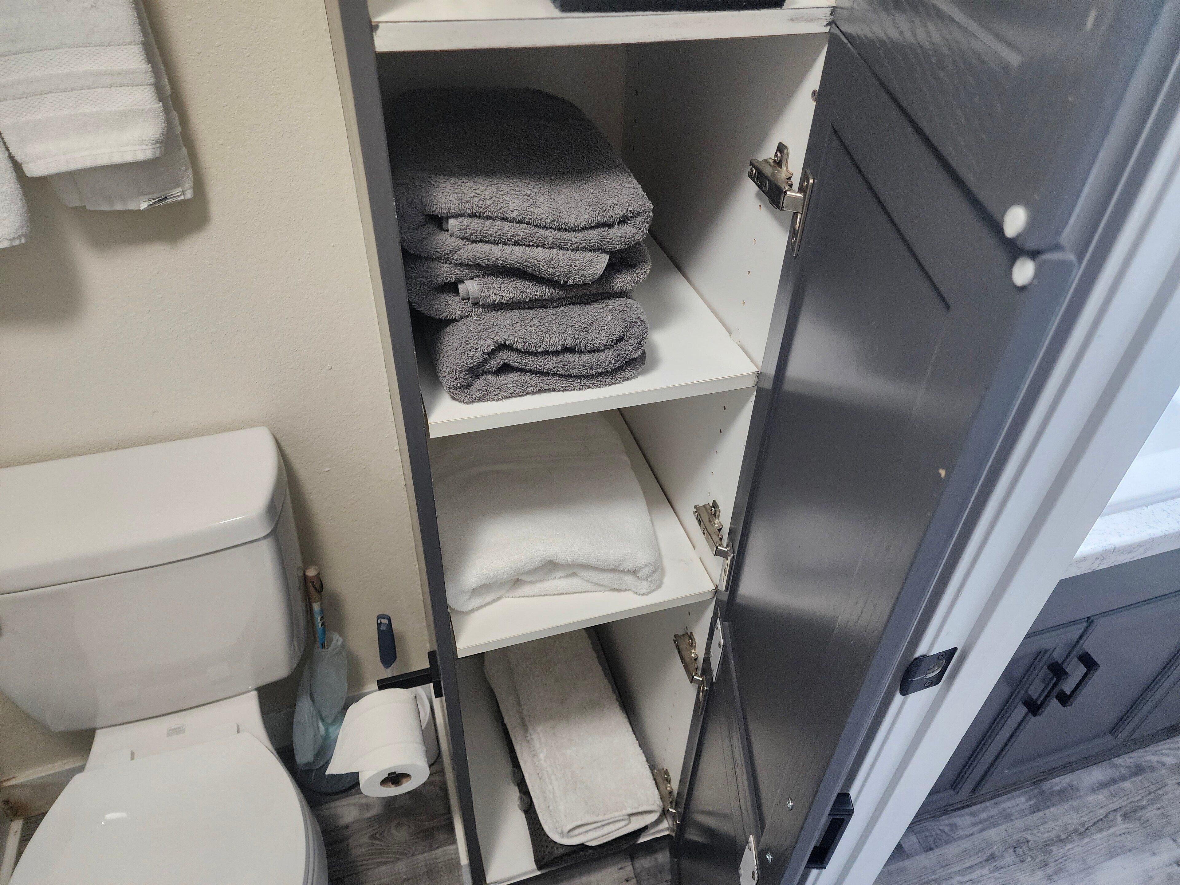 Un baño con un inodoro, un estante con toallas dobladas y un rollo de papel higiénico.
