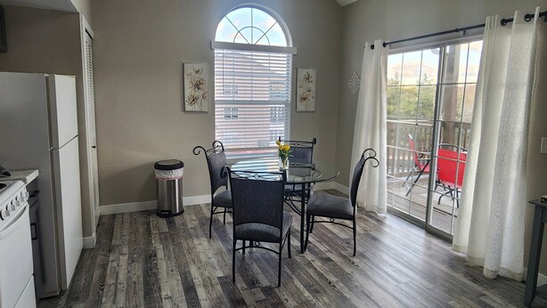 Una cocina con una mesa de comedor y sillas, un cubo de basura y una ventana con persianas.