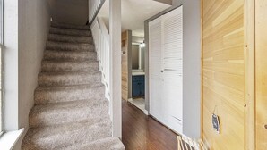 Eine Treppe führt zu einem Schlafzimmer mit einer Holztür, im Hintergrund ist ein Badezimmer zu sehen.
