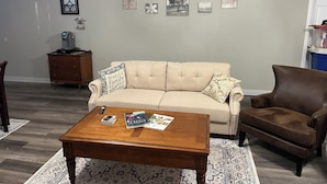 Una sala de estar con un sofá color beige, un sillón de cuero marrón, una mesa de centro de madera y un tapete estampado.