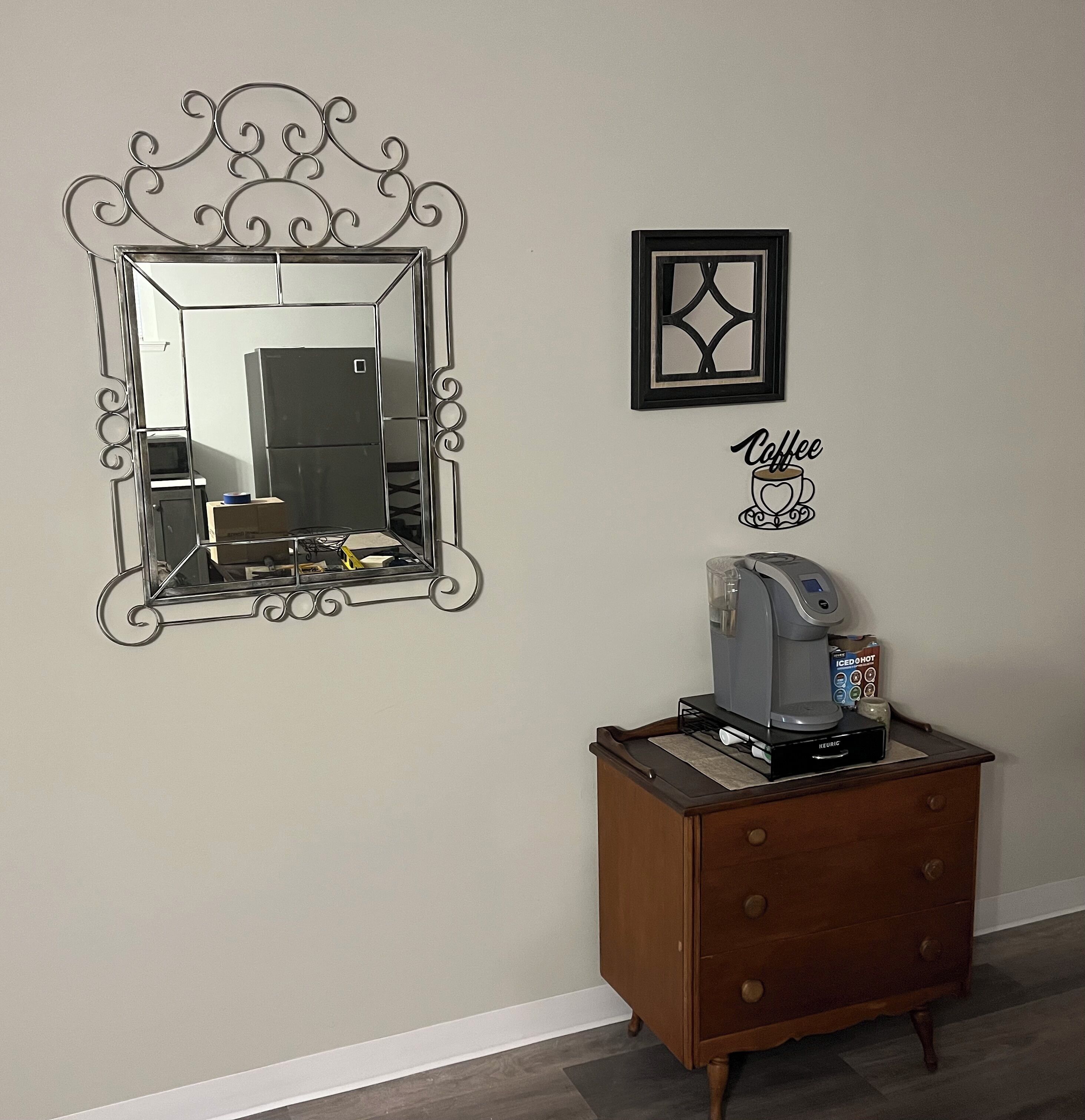 Une pièce avec un miroir, un tableau encadré, une machine à café et une commode en bois.