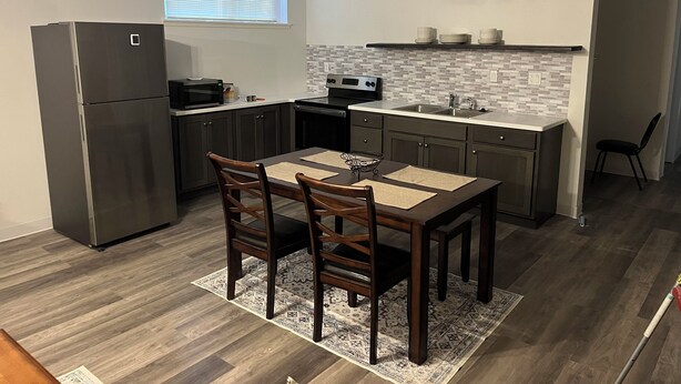 Una cocina compacta con refrigerador, microondas, estufa y pileta. Hay una mesa de comedor con sillas y un alfombra estampado.