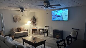 Una sala de estar con sofá, mesa de centro, sillas, chimenea, televisor y ventilador de techo.