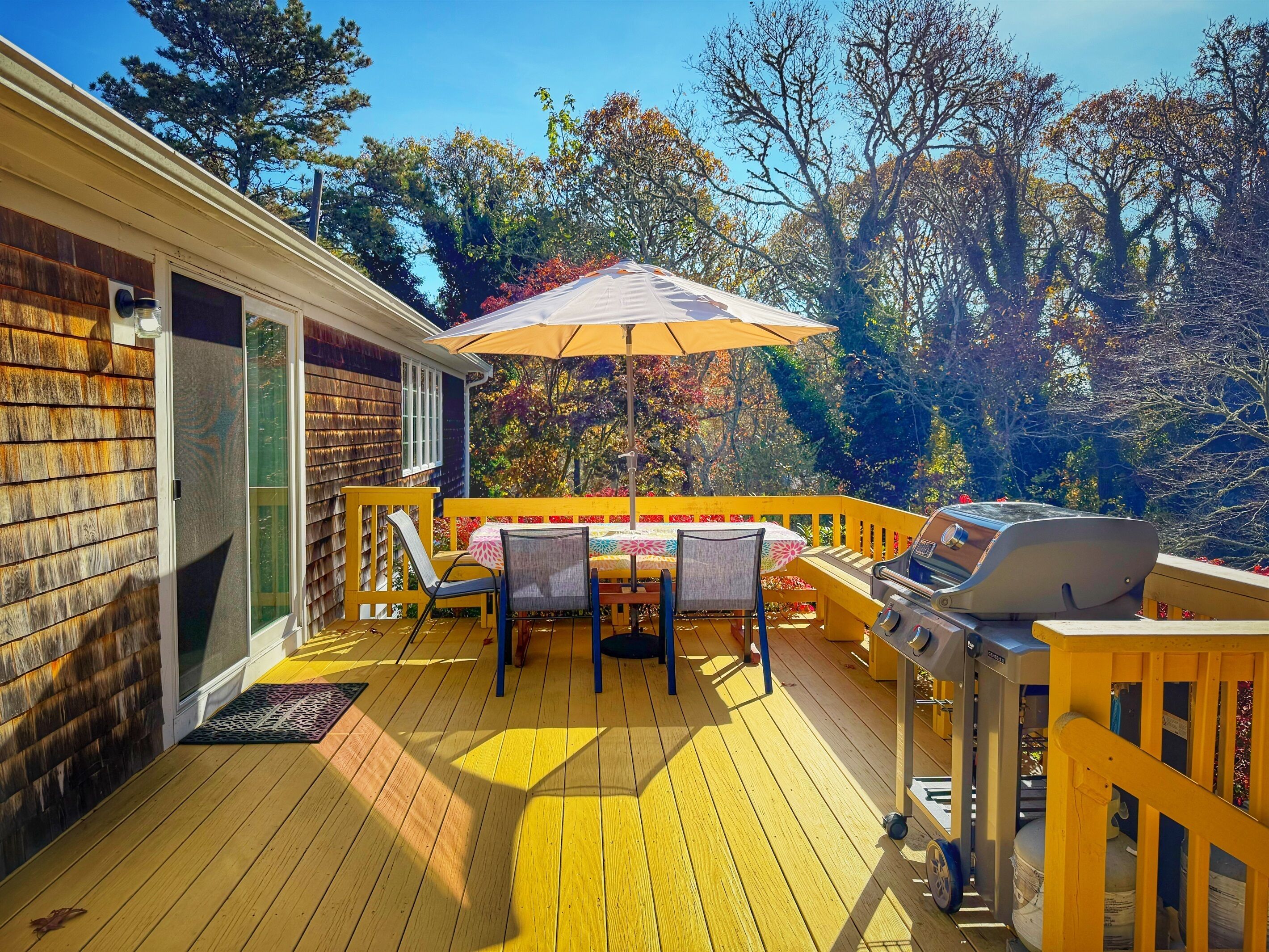 A wooden deck with a grill, outdoor furniture, and a view of trees.