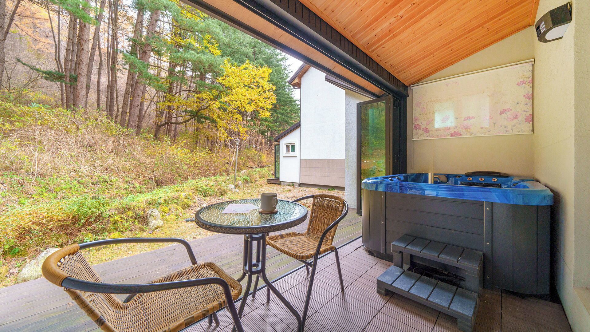 A patio with a hot tub, wicker chairs, and a glass table.