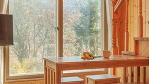 A wooden dining table with a white mug and tulips, set against a window with a view of trees and a fence. - Gapyeong Sanchaek Glamping Pension (Gapyeong)