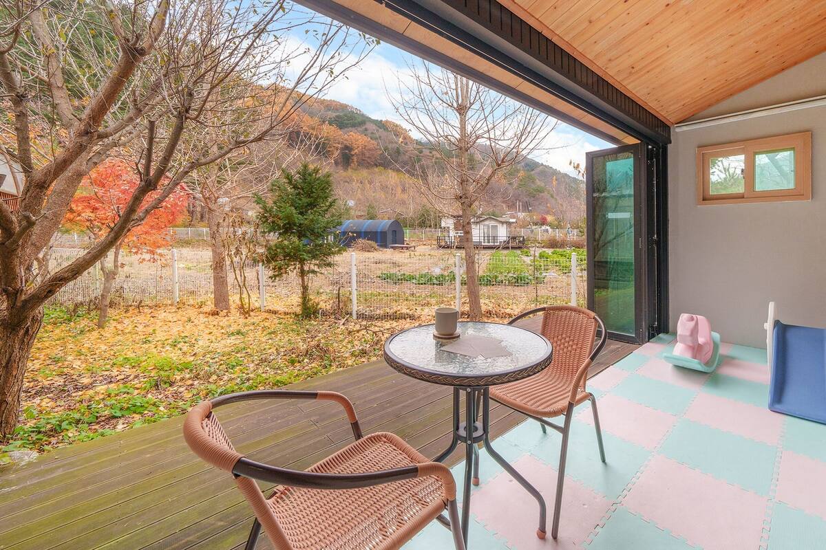 Ein Balkon mit Tisch und Stühlen, ein Spielbereich mit Rutsche und Blick auf Garten und Hügel.