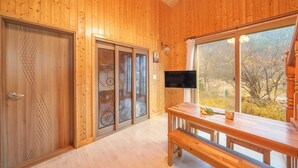 A wooden interior with a sliding glass door, a wooden bench, a table with a bouquet, and a TV mounted on the wall. - Gapyeong Sanchaek Glamping Pension (Gapyeong)
