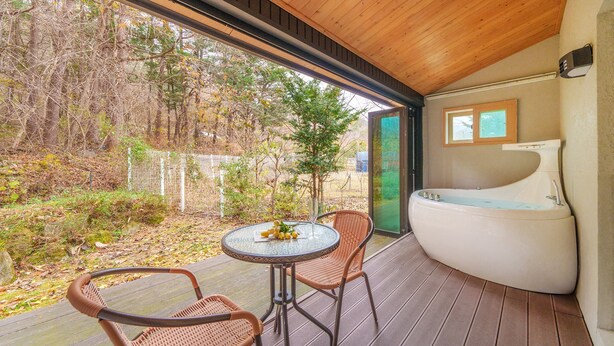 A modern outdoor seating area with wicker chairs and a glass table, a large bathtub, and a view of a forested area. - Gapyeong Sanchaek Glamping Pension (Gapyeong)