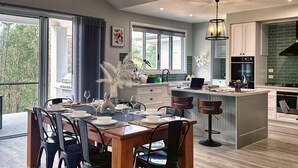 A modern kitchen with a central island, a dining area with a wooden table and chairs, and large windows providing natural light. - Luxury Home for Work Teams and Families (Muswellbrook)