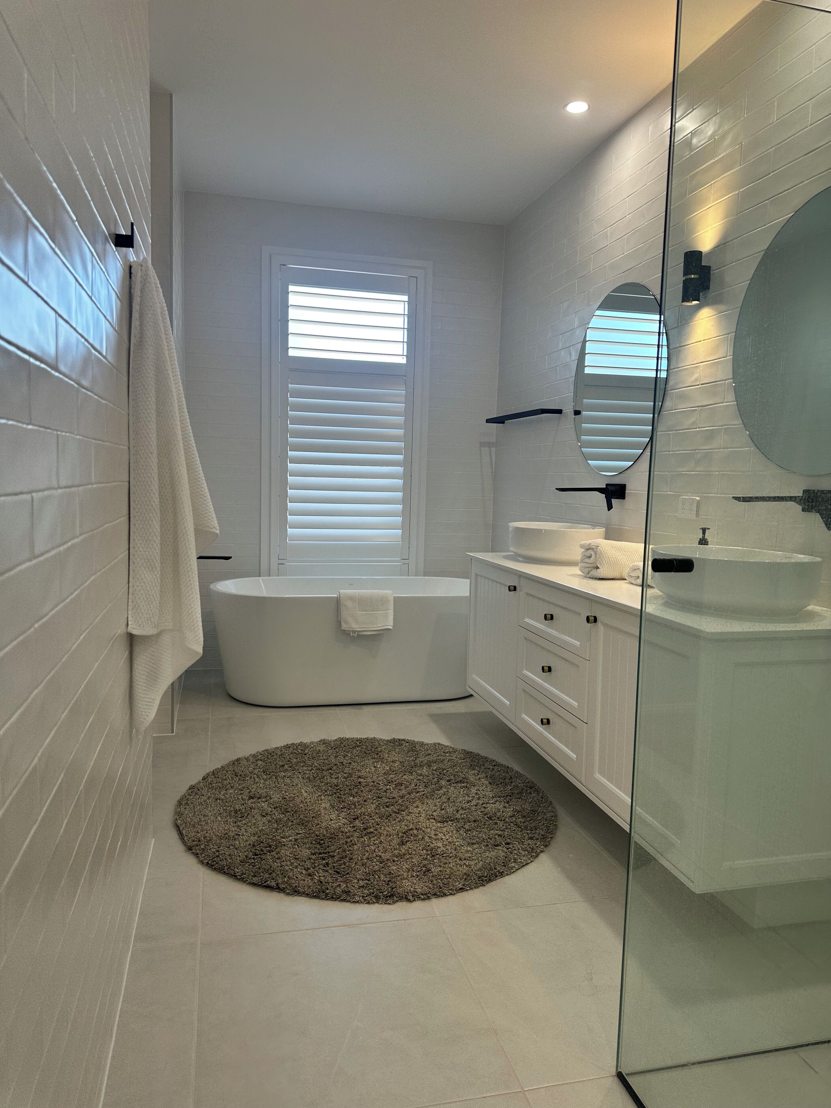A modern bathroom with a bathtub, a large mirror, and a round rug.