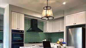 A modern kitchen with white cabinetry, a central island with bar stools, a stainless steel refrigerator, and a black range hood. - Luxury Home for Work Teams and Families (Muswellbrook)