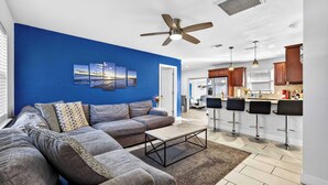 A modern living room with a blue accent wall, a gray sectional sofa, a coffee table, and a ceiling fan.