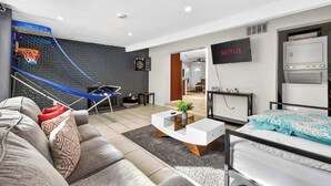 A modern living room with a grey sofa, a white coffee table, a bed, and a TV mounted on the wall.