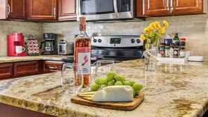 A kitchen with wooden cabinets, a stainless steel microwave, a red coffee maker, a bottle of Barefoot Pink Oscato wine, a glass of wine, and a cutting board with cheese and grapes.