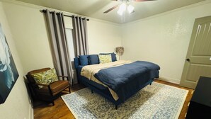 A bedroom with a bed, a chair, a ceiling fan, and a door.