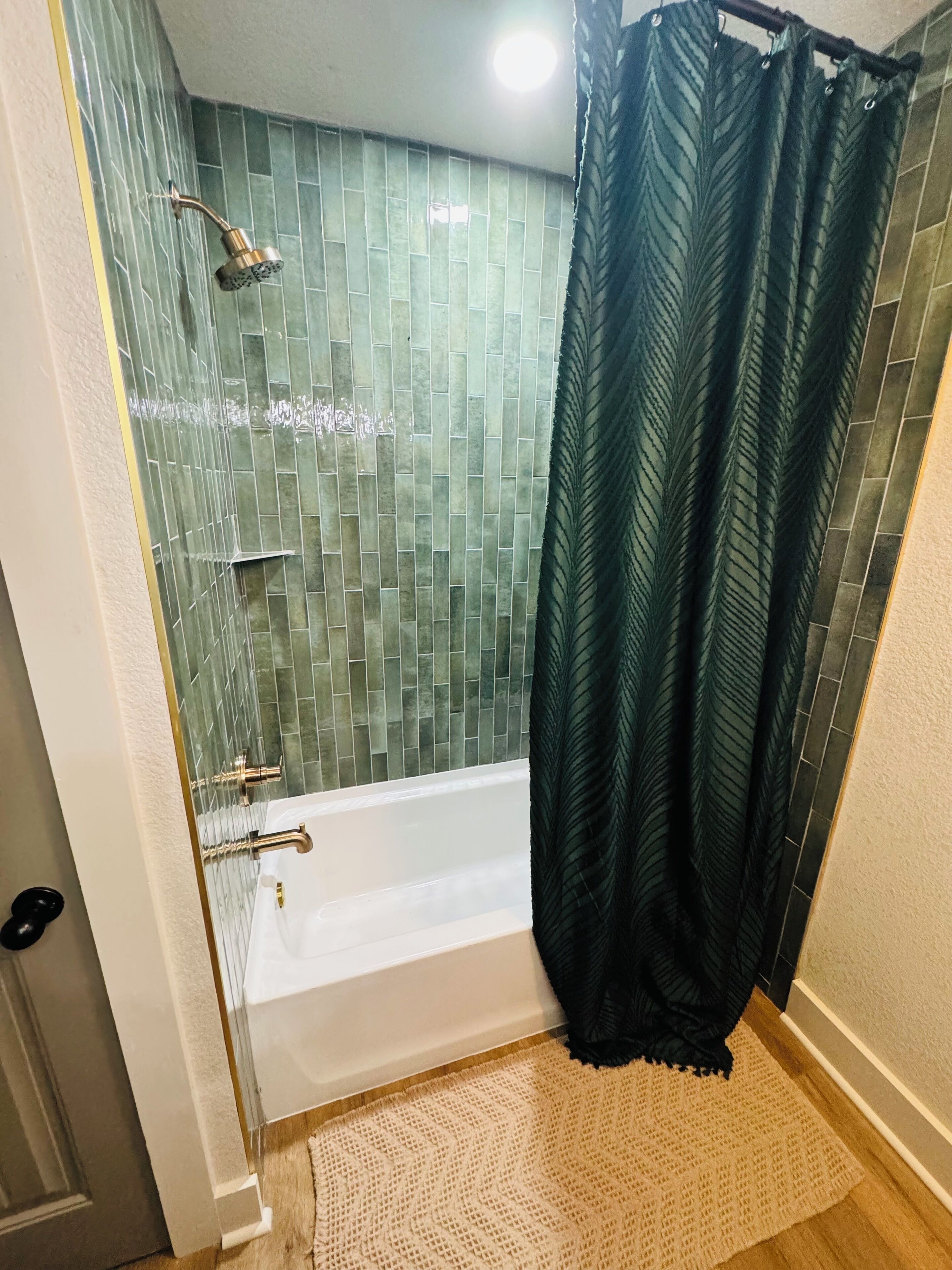Un bagno con una vasca, una doccetta e un muro rivestito di piastrelle verdi.