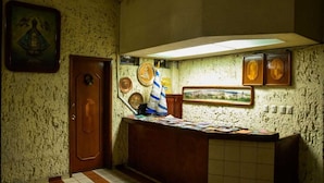 Een klein receptiegedeelte met een houten deur, betegelde vloer, een balie met papieren en een wand met ingelijste foto's en plaquettes.