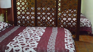 Een kamer met een bed bekleed met beddengoed met een patroon, een houten scheidingswand en een lamp op een nachtkastje.