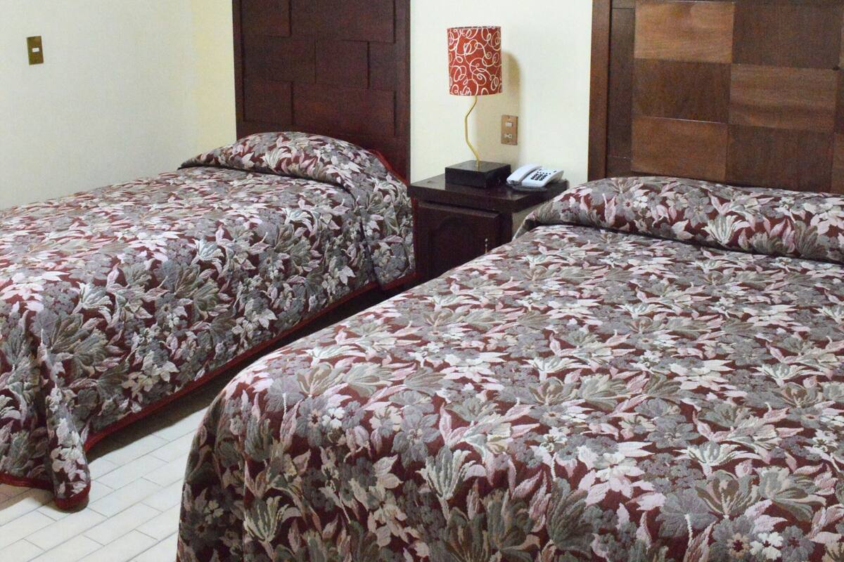 Una habitación con dos camas, cada una con ropa de cama de estampado floral, un cabecero de madera y una mesita de noche con una lámpara y un teléfono.