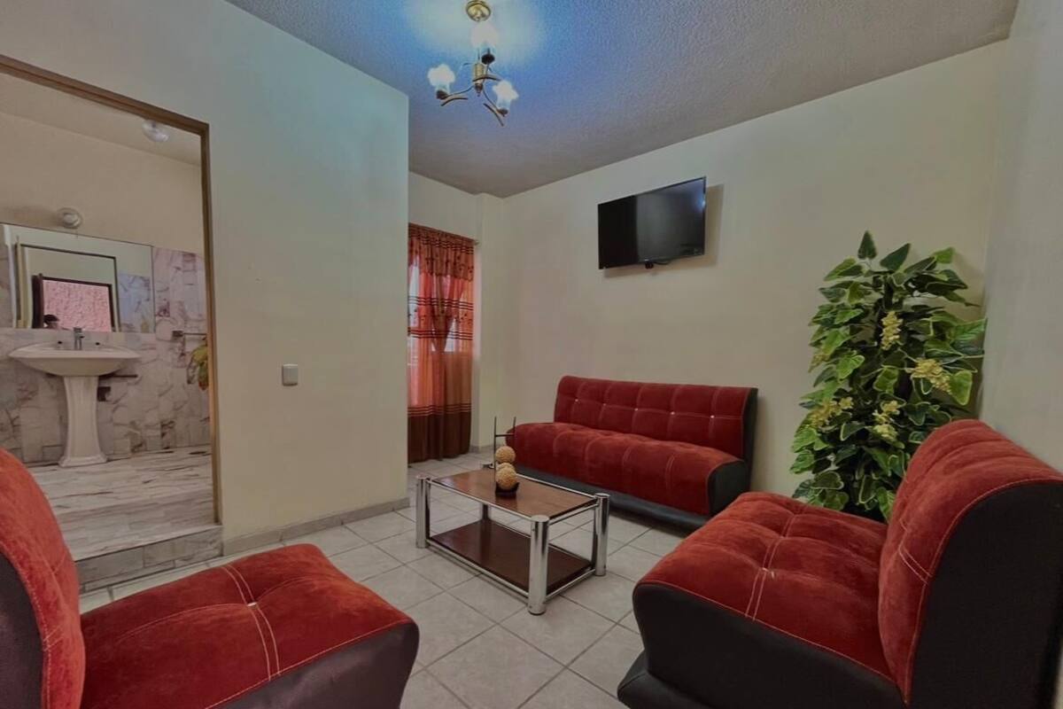 Un salón con un sofá rojo, una mesa de centro, un televisor montado en la pared y una planta en maceta.
