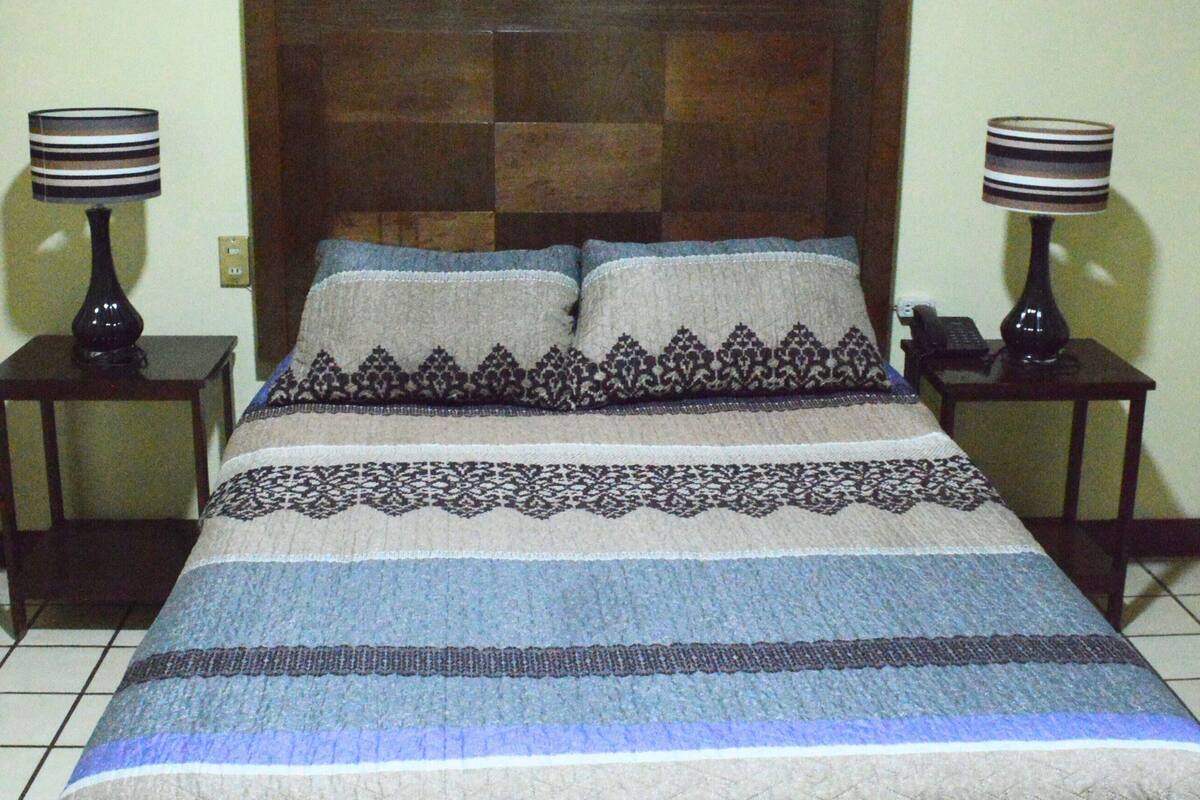Una cama con colcha acolchada y dos almohadas, con dos mesitas de noche y lámparas a cada lado.