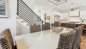 Eine moderne Küche mit weißen Schränken, einem Edelstahlkühlschrank und einem Essbereich mit einem Glastisch und gemusterten Stühlen.