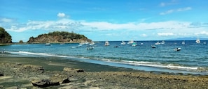 A coastal scene with boats on the water and rocky terrain in the foreground.