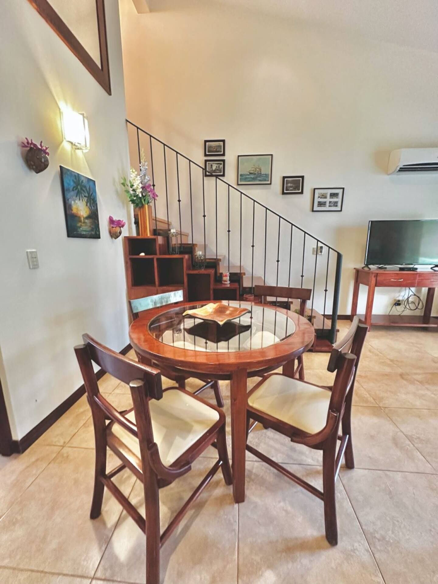 A dining area with a round wooden table and chairs, a staircase with a railing, and a television on a stand.