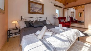 A bedroom with a large bed, a nightstand, a red chair, and a mirror.