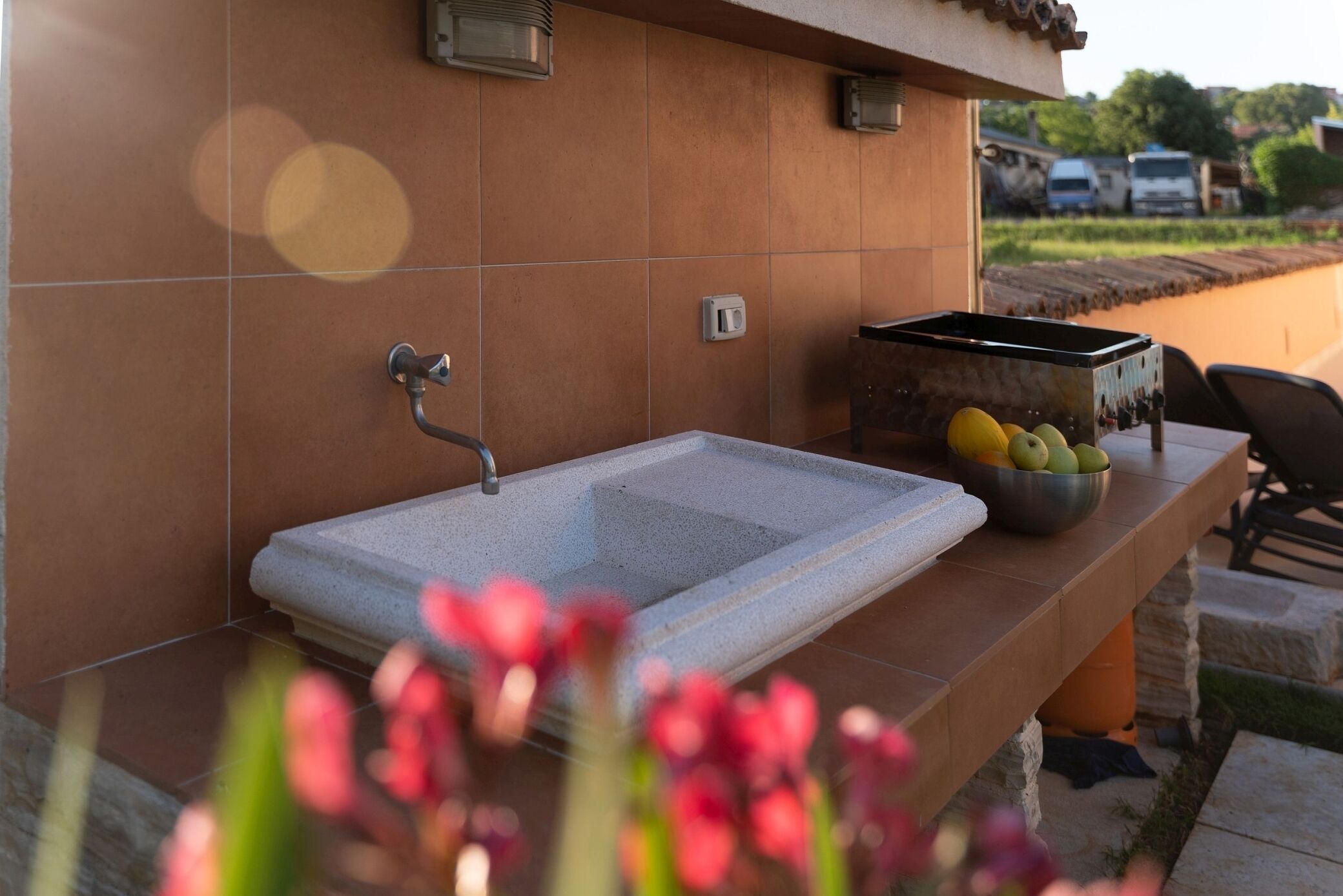 A stone sink with a faucet, a bowl of fruit, and a tiled wall.