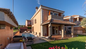 A two-story house with a swimming pool, outdoor seating area, and a well-maintained lawn.