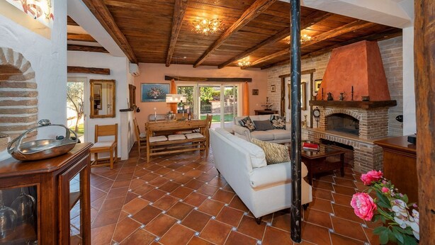 A cozy living room with a fireplace, wooden beams, and a tiled floor.