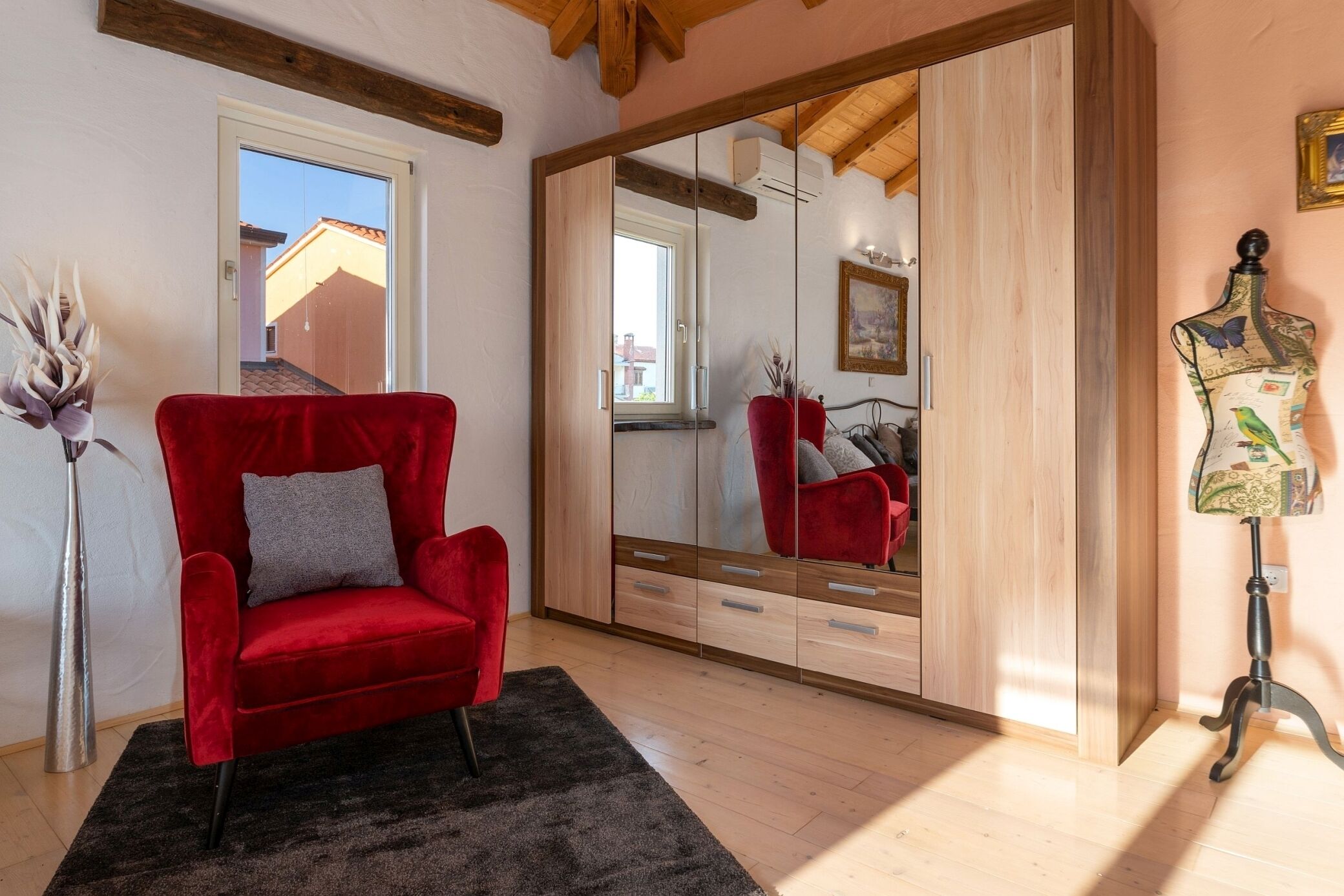 Una habitació amb una butaca de vellut vermell, un mirall gran, un armari de fusta i un maniquí.