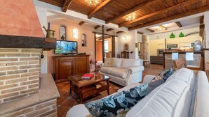 A cozy living room with a fireplace, a television, and a kitchen in the background.