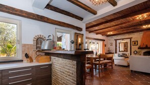 A kitchen with a brick wall, wooden beams, and a dining area with a white sofa and wooden chairs.