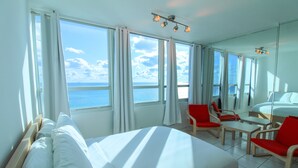 A hotel room with a large bed, two red chairs, a small table, and a view of the sea through large windows. - Castle 1133 Ocean view studio, Pool and Beach Access, FREE Parking, Gym, Tennis and more! (Miami Beach)