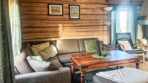 A cozy room with a wooden log wall, a sofa with cushions, a wooden table, and two framed pictures.