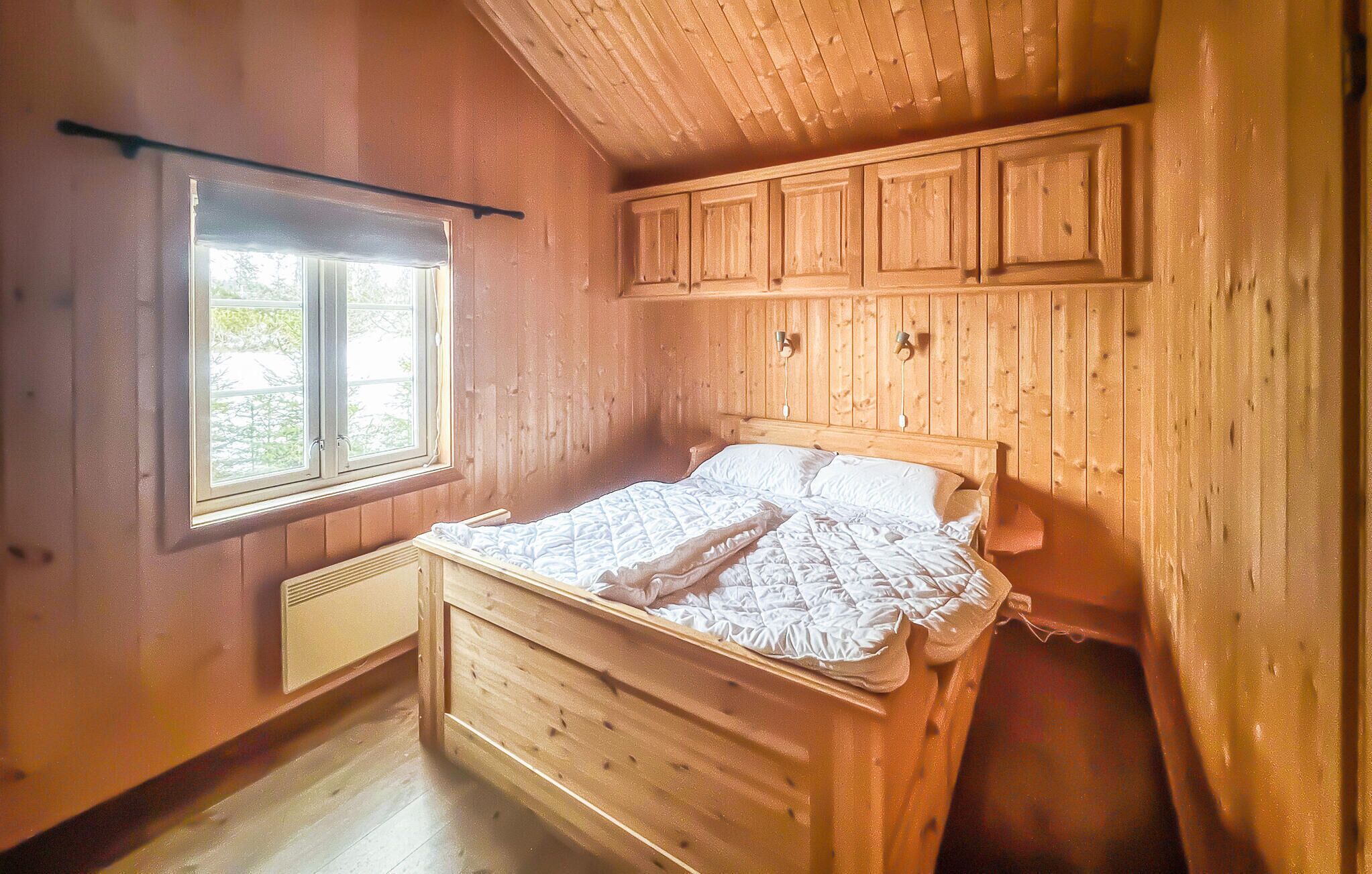 A wooden room with a bed, a window, and wooden paneling on the walls.