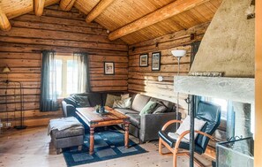 Interior de una cabaña de troncos con un sofá, una mesa de madera y una chimenea.