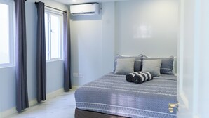 A bedroom with a bed, curtains, an air conditioning unit, and a window. - Caldera Villas Where Nature Meets Comfort (Soufriere)