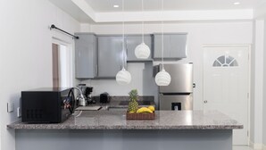 A modern kitchen with grey cabinets, a granite countertop, a black microwave, a fruit basket, and pendant lights. - Caldera Villas Where Nature Meets Comfort (Soufriere)