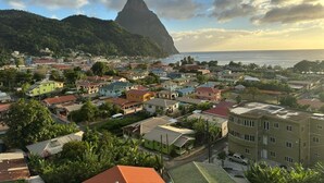 A coastal town with buildings, a prominent mountain, and the ocean. - Caldera Villas Where Nature Meets Comfort (Soufriere)