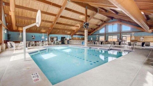 An indoor swimming pool with a high ceiling and wooden beams, surrounded by lounge chairs and a clear view of the sky.