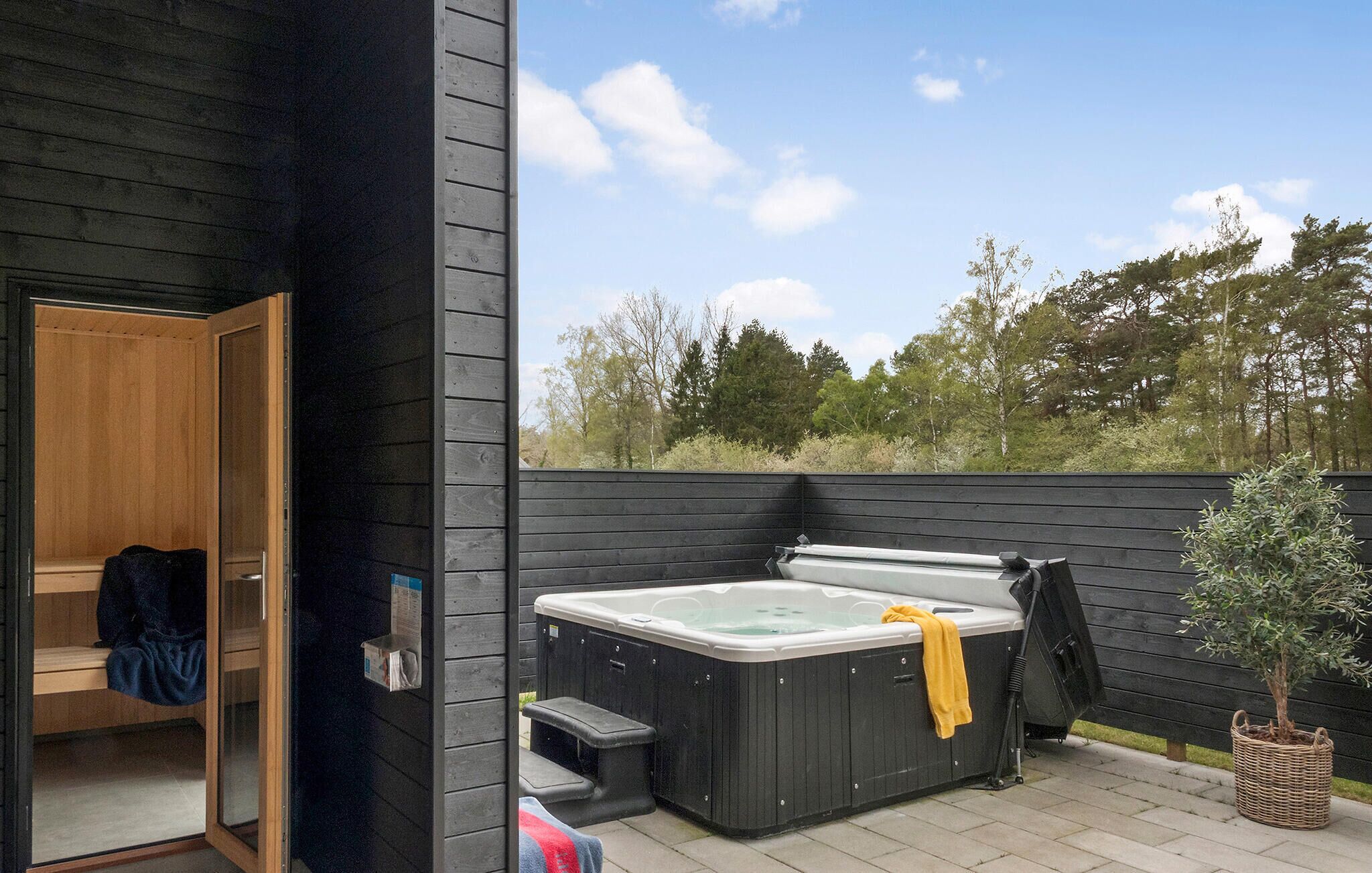 Een wellnessruimte met een jacuzzi, houten banken en een kleine boom.